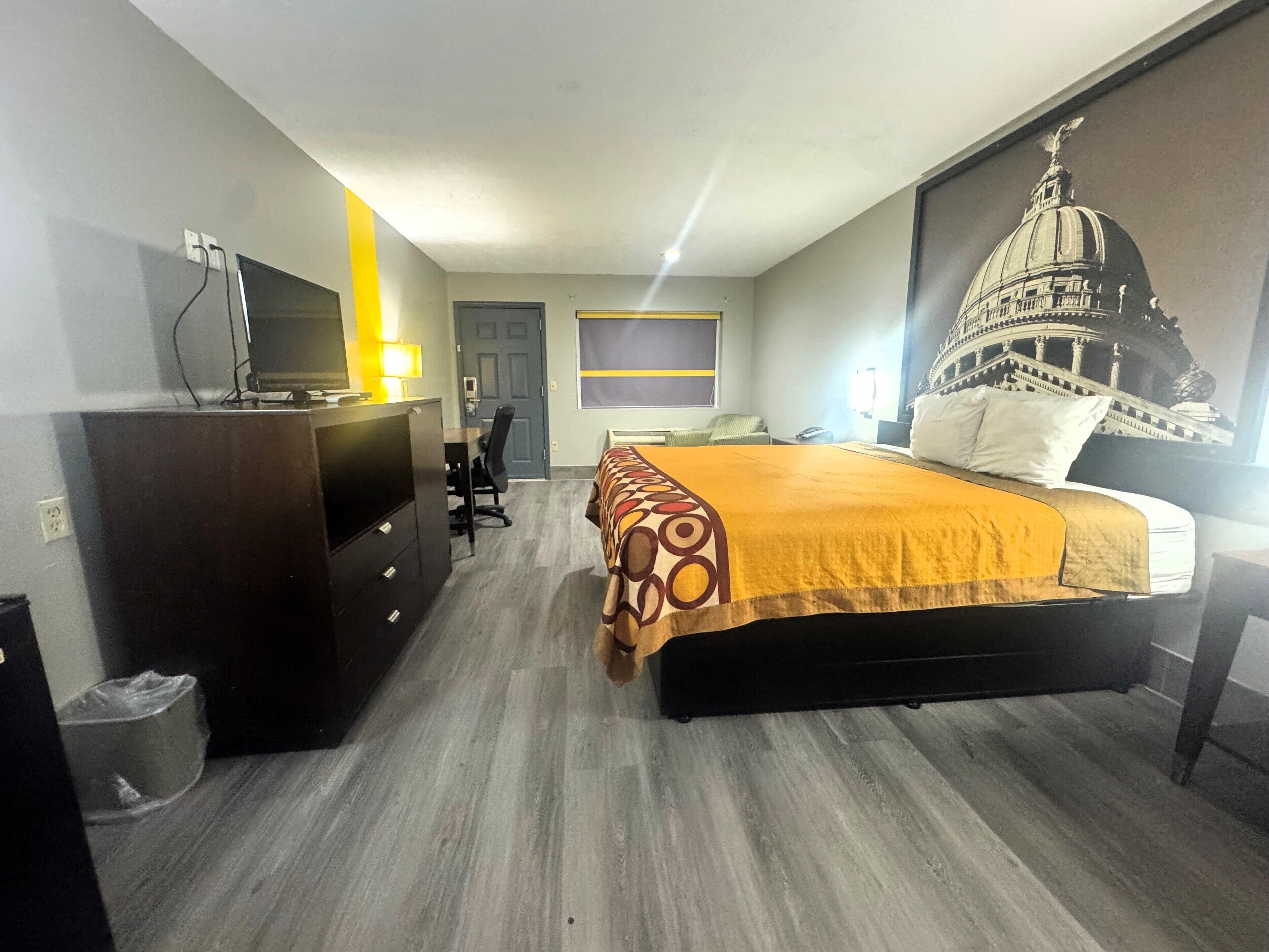 A hotel room with a bed, a desk, a chair, a TV, and a wall with a mural.