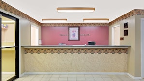 Een receptiegedeelte met een roze muur, een ingelijst kunstwerk en een receptiebalie.