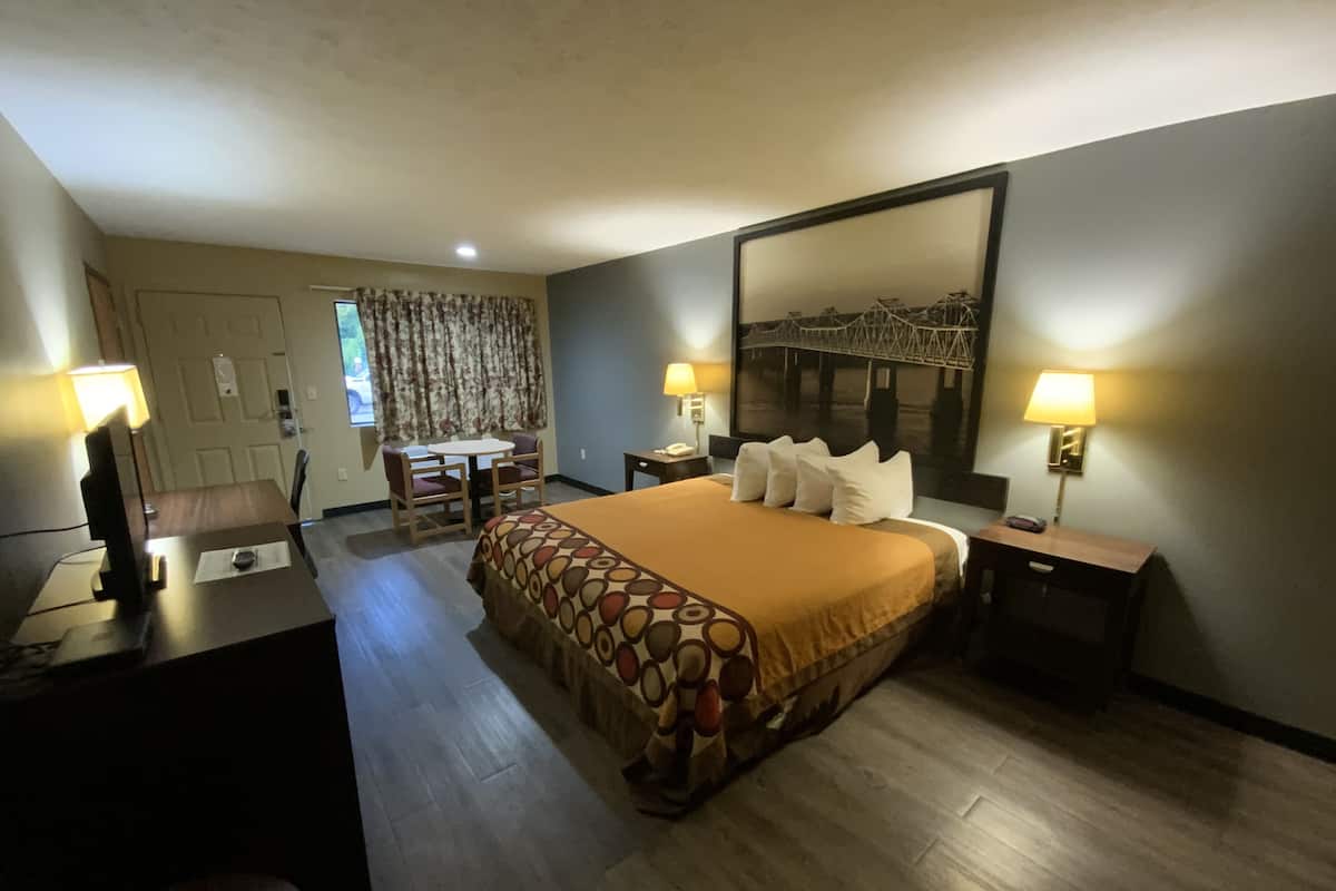 Ein Hotelzimmer mit einem großen Bett, zwei Nachttischen, einem Schreibtisch mit Stuhl und einem fenster mit Vorhängen.