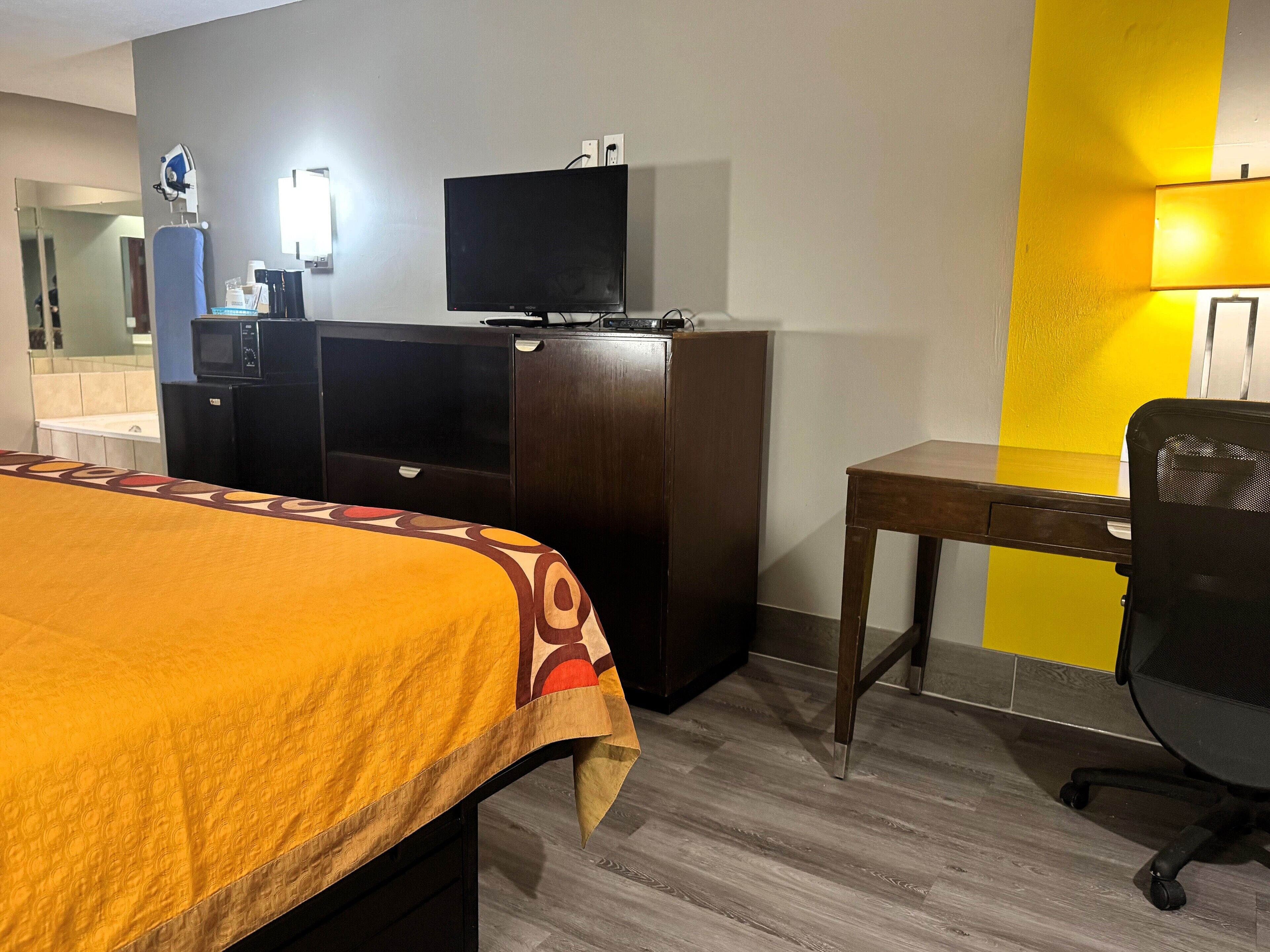 A hotel room with a bed, a desk, a chair, a television, and a microwave.