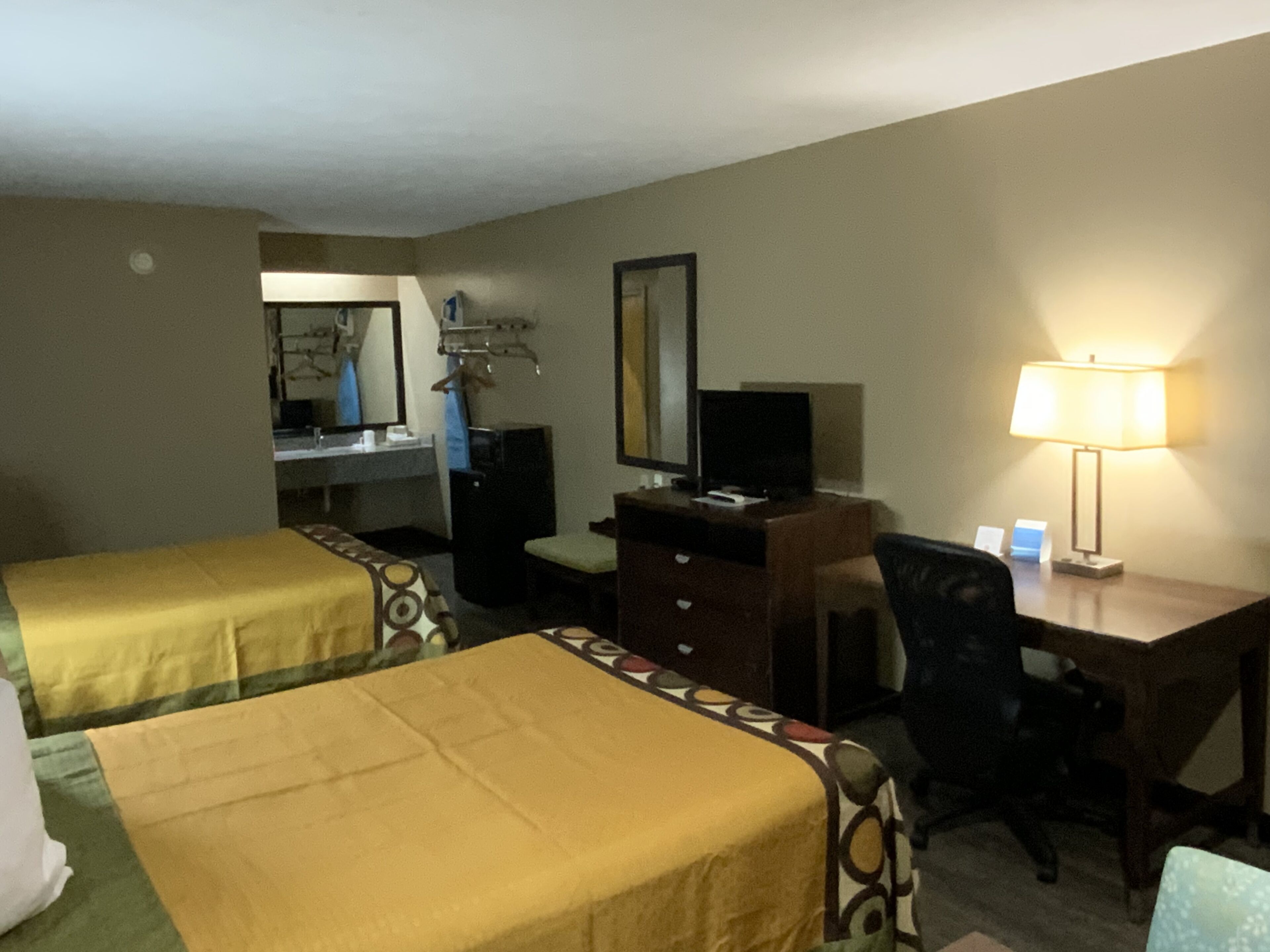 A hotel room with two single beds, a desk with a chair, a television, a desk lamp, and a mirror.