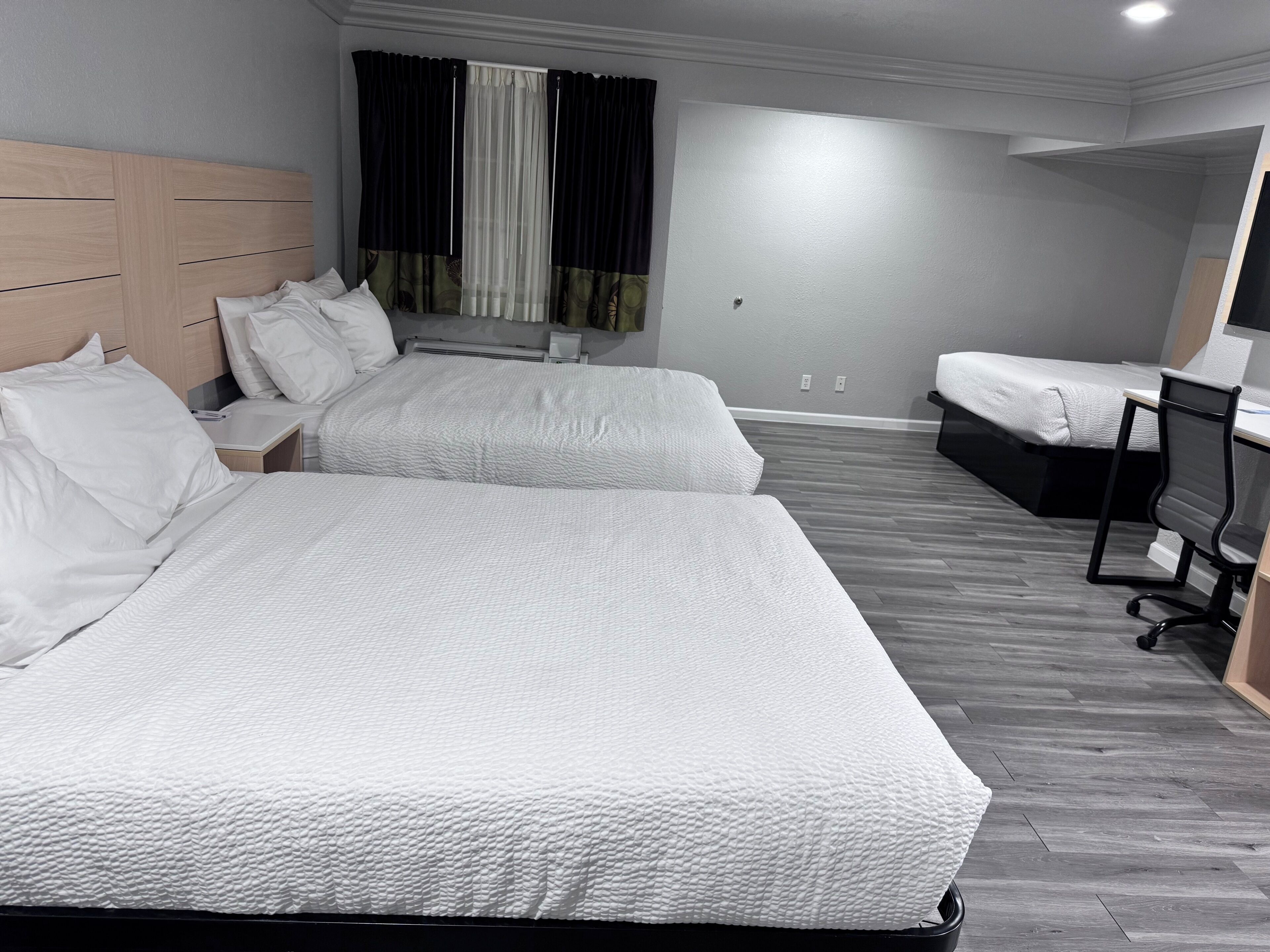 A hotel room with two beds, a desk, a chair, and a window with curtains.