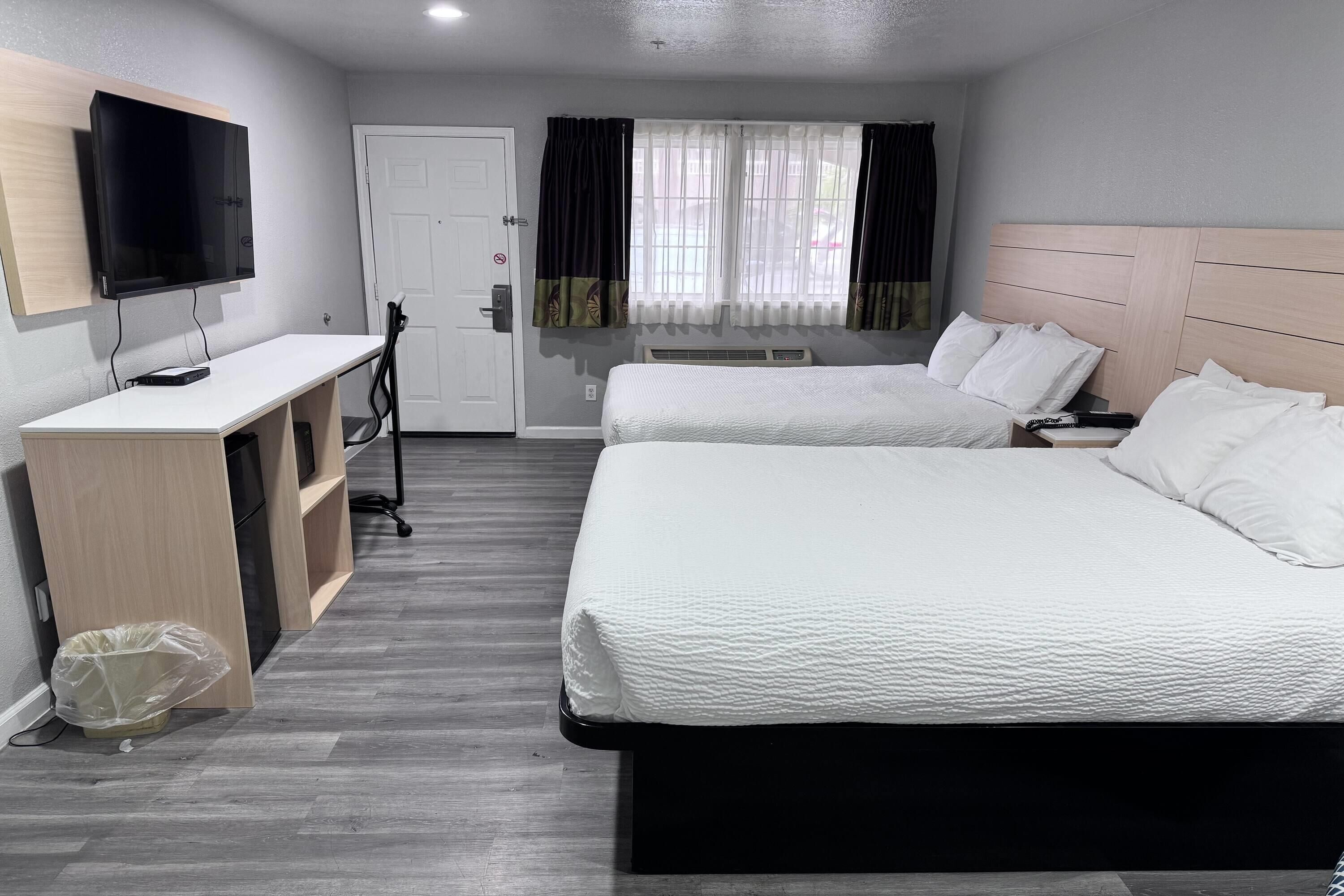 A hotel room with a bed, a desk, a TV, and a window with curtains.