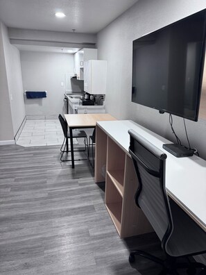 Un espacio de oficina moderno con un escritorio largo, una silla, un televisor y una kitchenette al fondo.