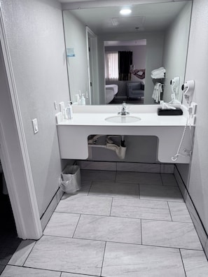A modern bathroom with a large mirror, white sink, and a hairdryer.