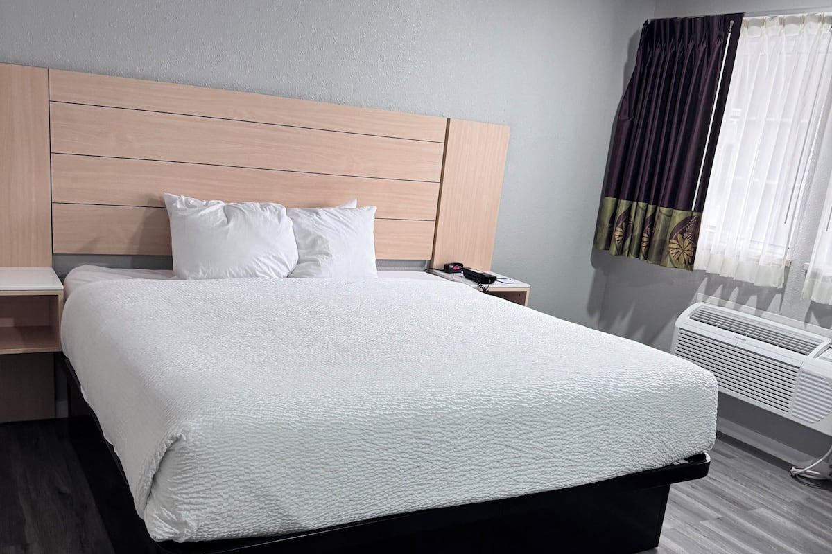 Une chambre dâhĂŽtel avec un lit, une table de chevet, un radiateur fixĂ© au mur et une fenĂȘtre avec des rideaux.