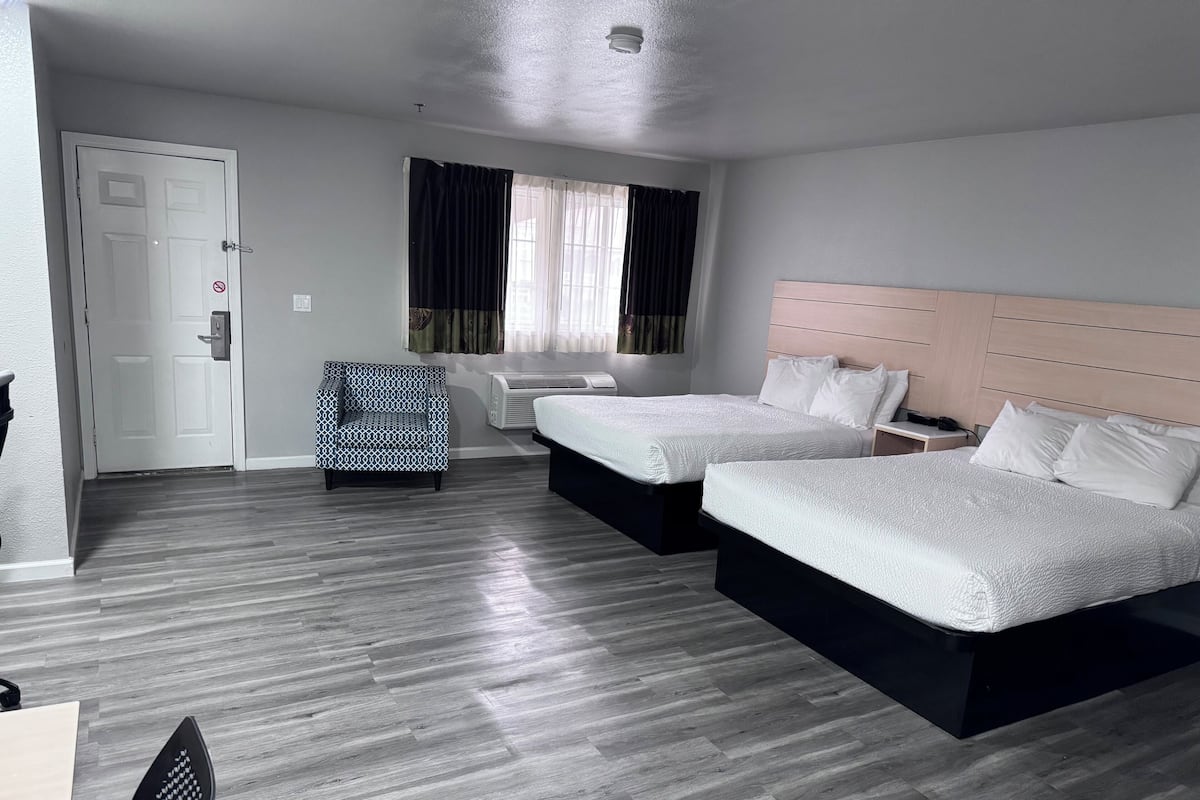 Une chambre dâhĂŽtel avec deux lits, un bureau, une chaise, une porte et une fenĂȘtre avec des rideaux.