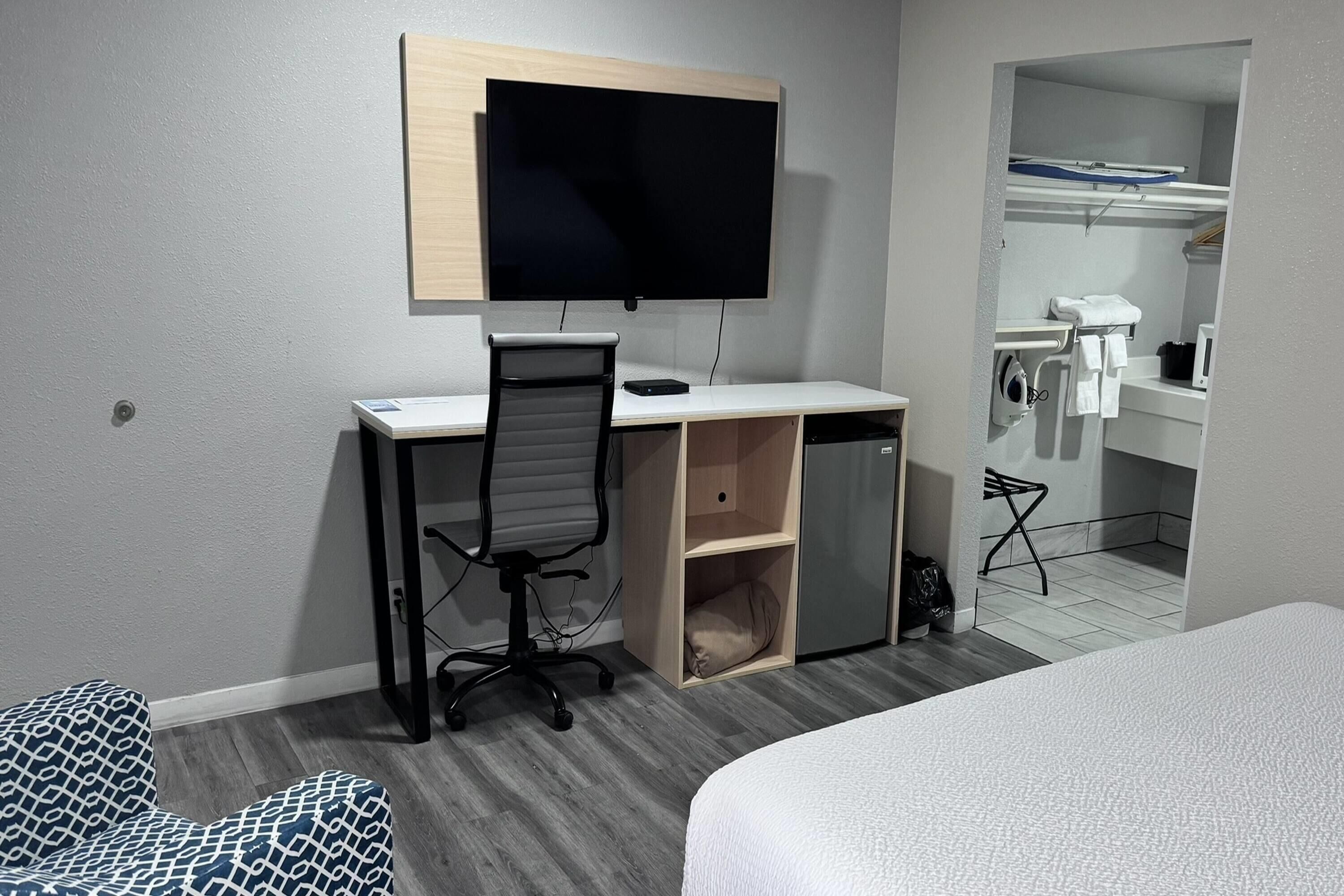 A bedroom with a bed, a desk with a chair, a TV, and a bathroom visible through an open door.