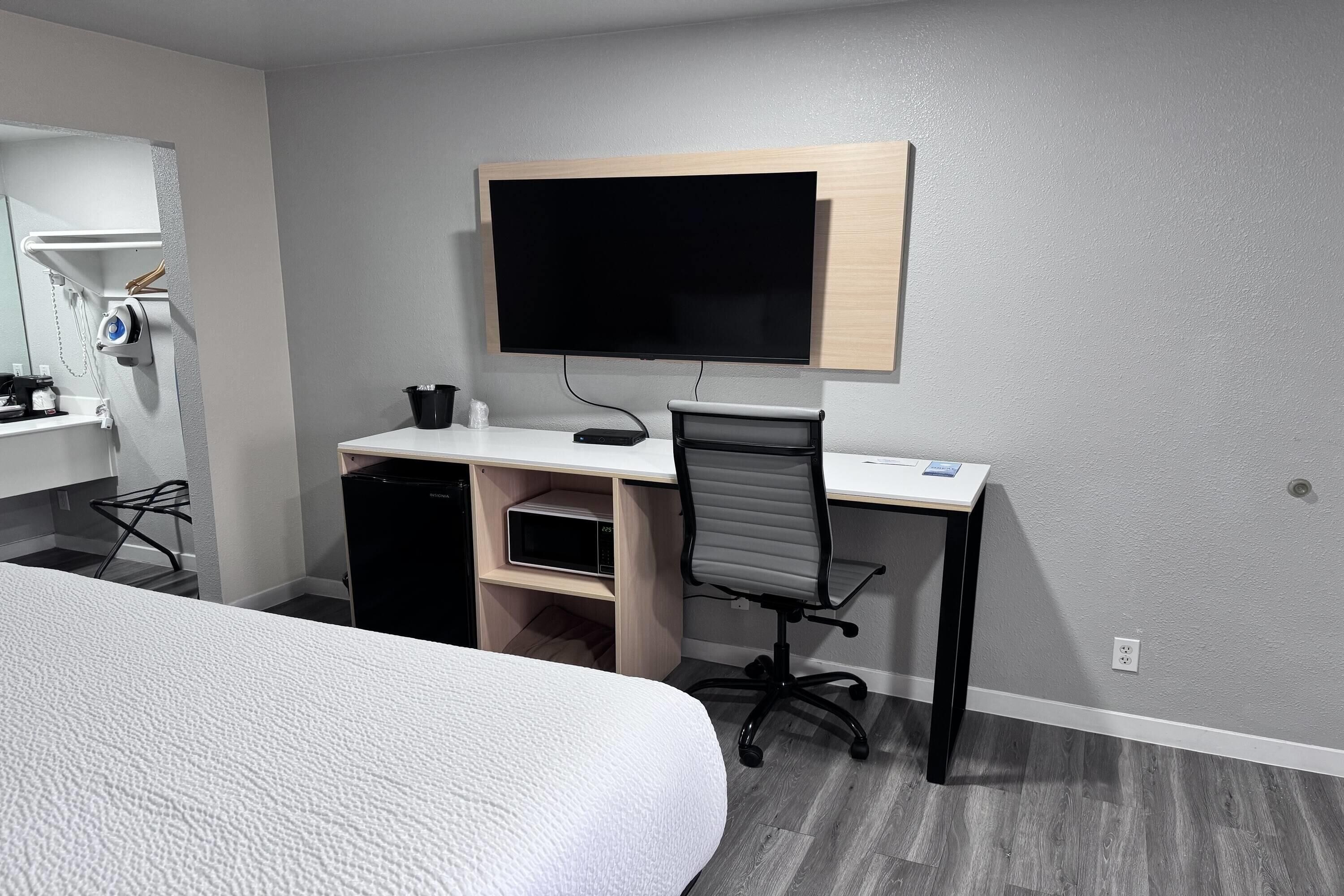 A hotel room with a bed, a desk with a computer, a chair, a TV, and a small cabinet.