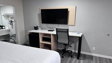A hotel room with a bed, a desk with a computer, a chair, a TV, and a small cabinet.