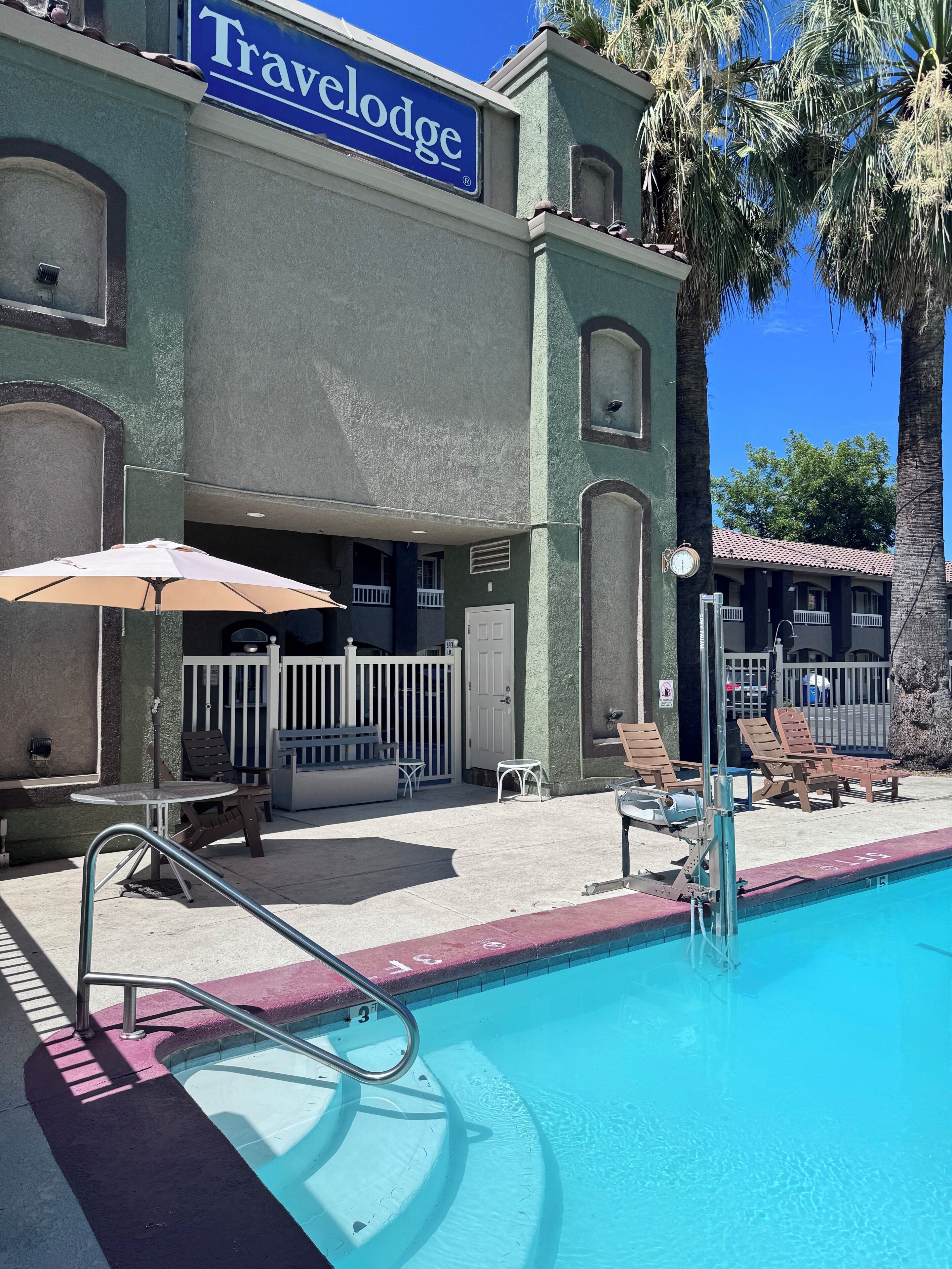 Edificio Travelodge con piscina, mobiliario exterior y valla blanca.