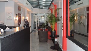 A modern reception area with a glass ceiling, a reception desk, seating area, and potted plants. - Hotel Eden Opéra (Paris)