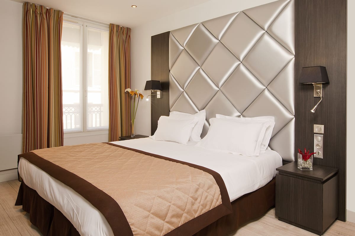 Une chambre d’hôtel avec un grand lit, une table de chevet et une lampe fixée au mur.