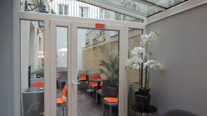 A glass-enclosed patio area with wicker furniture and potted plants. - Hotel Eden Opéra (Paris)