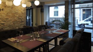 A restaurant with a stone wall, round pendant lights, and a view of a street with a car. - Hotel Eden Opéra (Paris)
