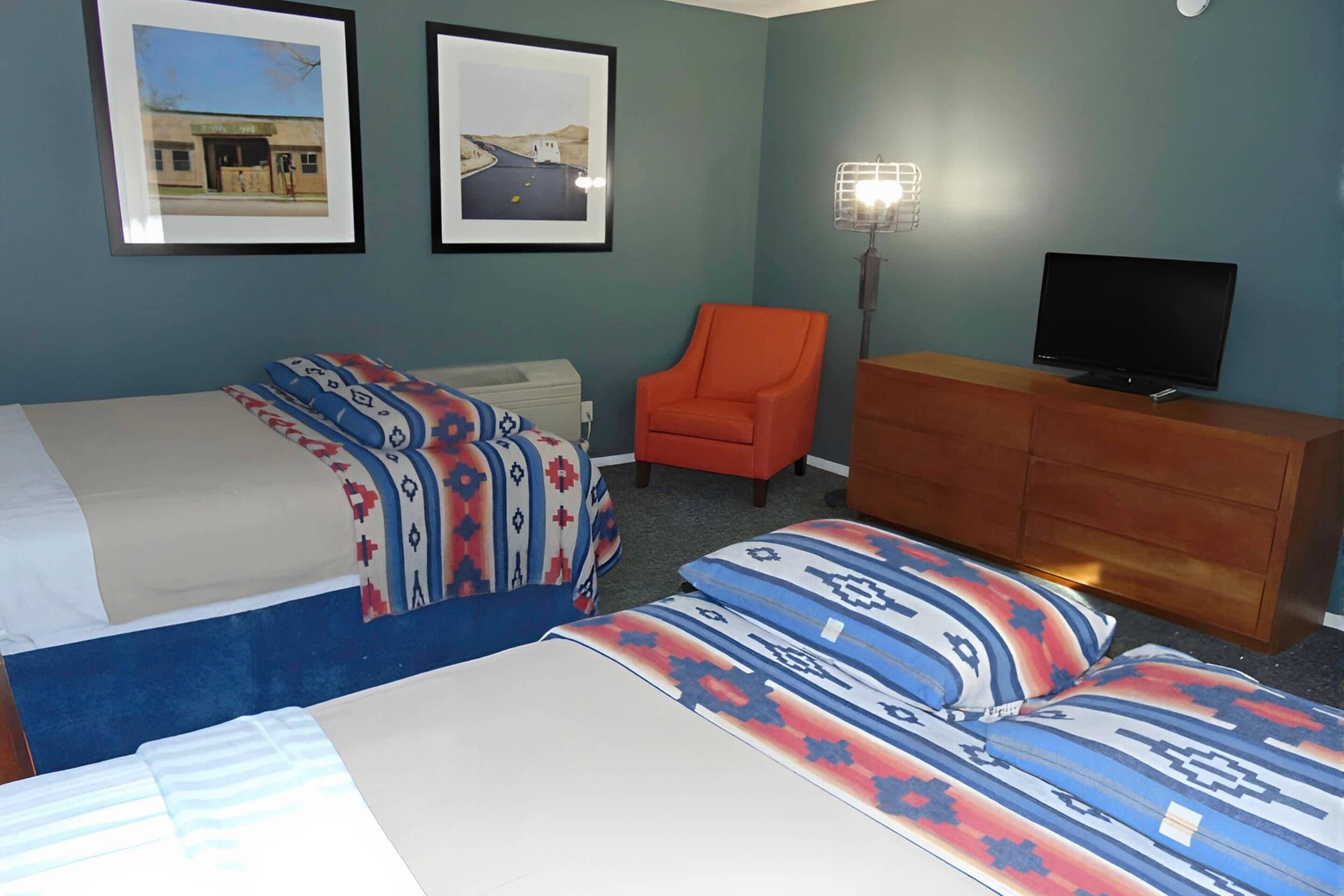 A hotel room with two beds, a television, a dresser, and two framed pictures on the wall.