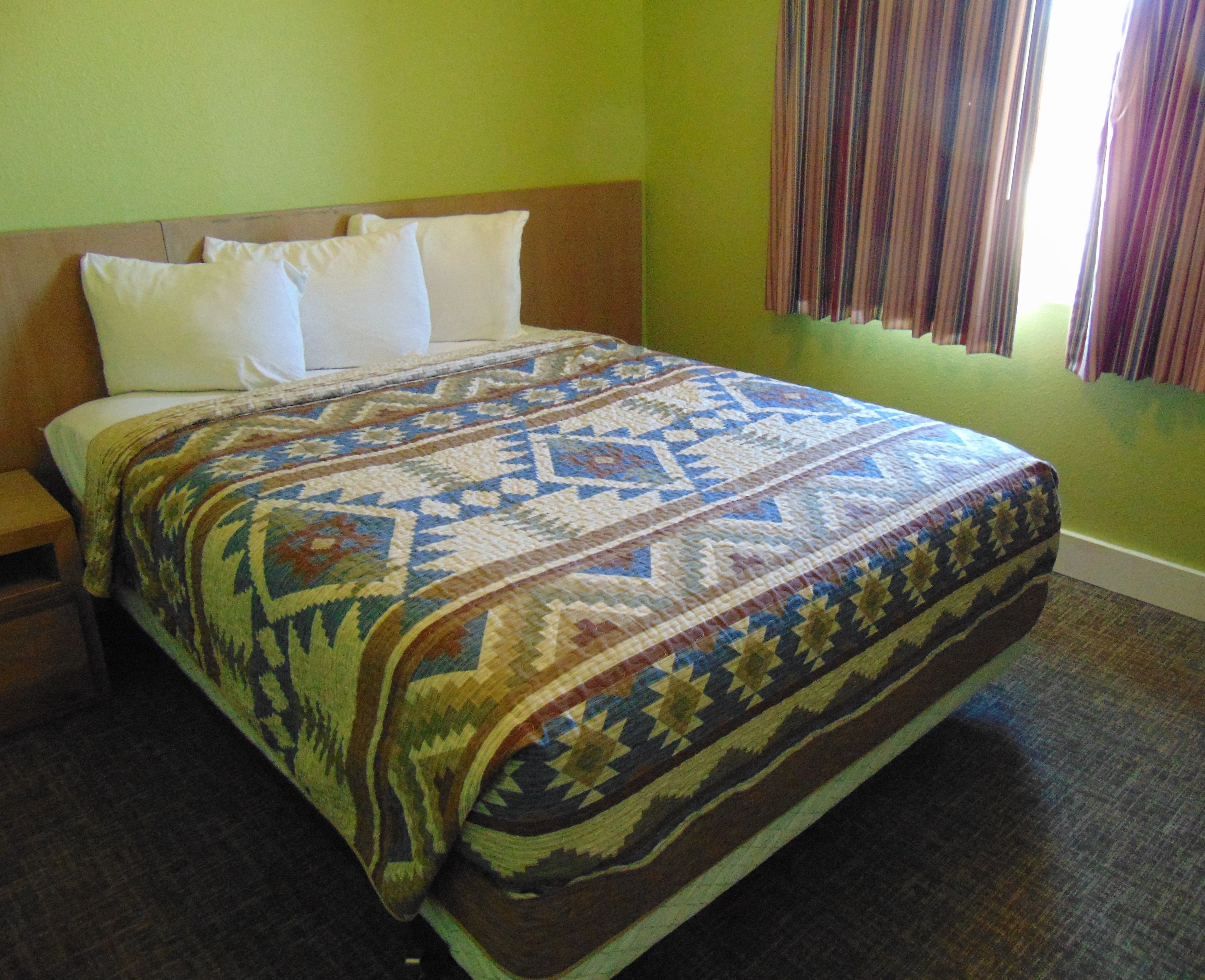 A neatly made bed with a patterned bedspread, a wooden headboard, and a nightstand with a lamp.