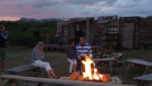 Entorno rústico al aire libre con fogata, bancos de madera y una pequeña estructura de madera con la leyenda 'STORE'.