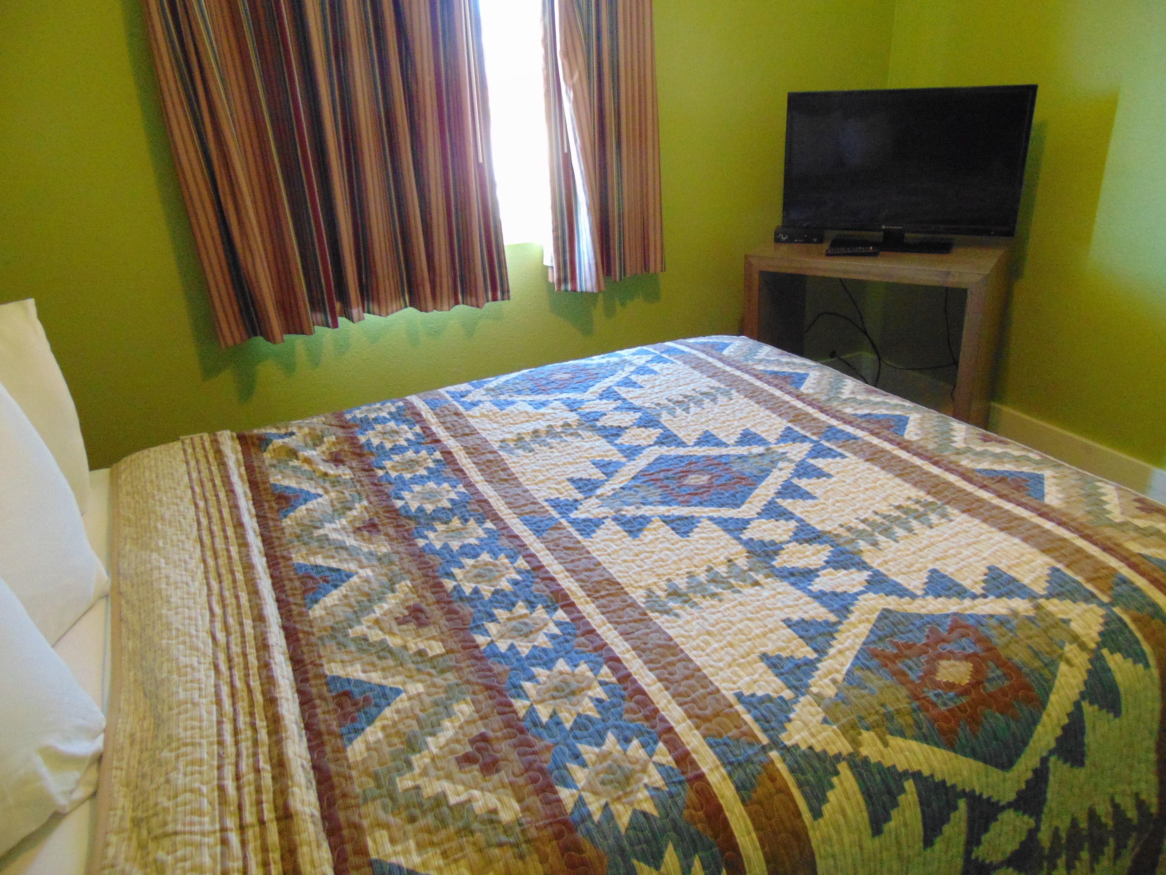 A room with a bed, a television on a stand, and curtains.