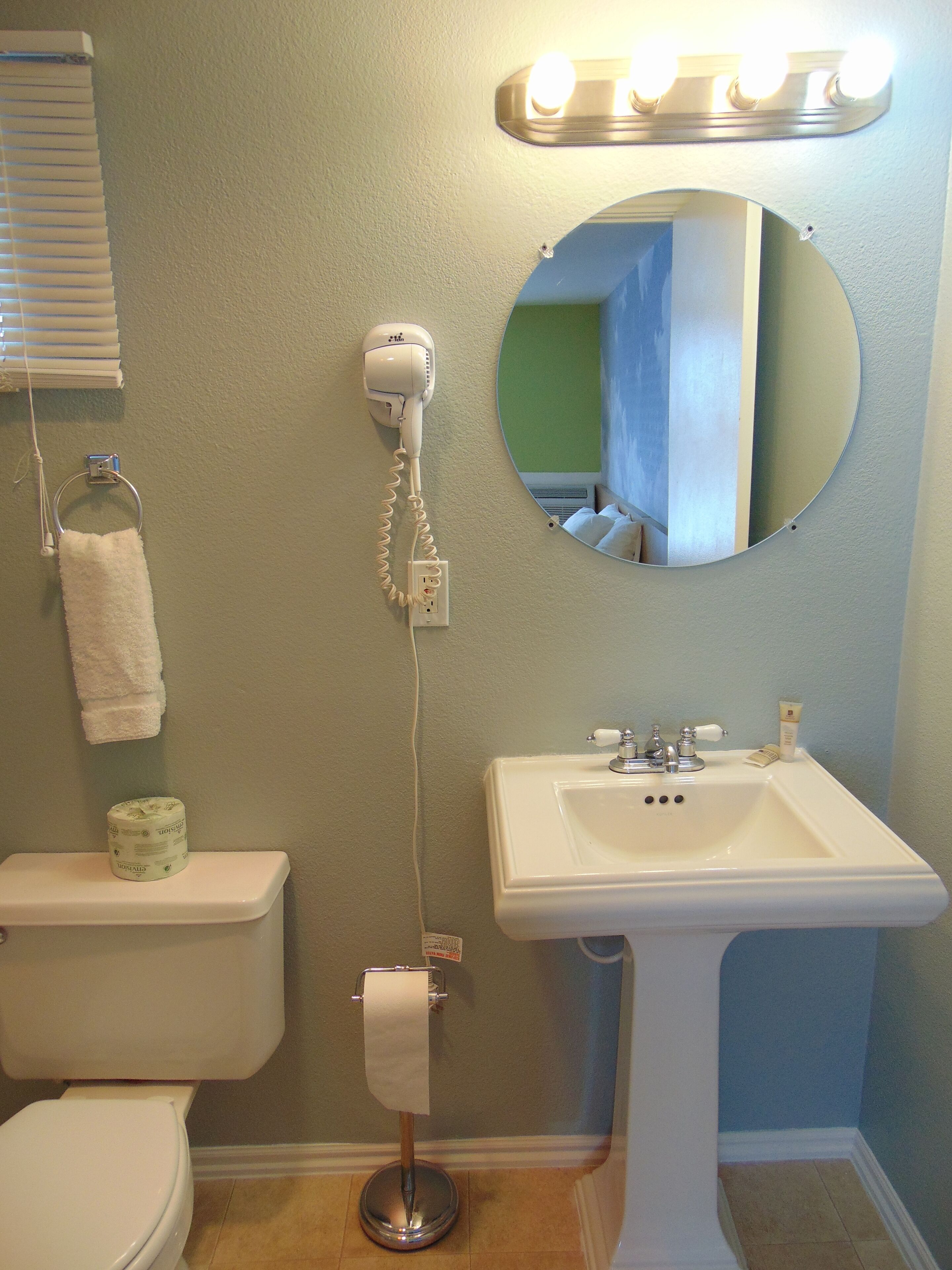 Un baño con inodoro, lavamanos, secador de pelo, toallero y espejo.