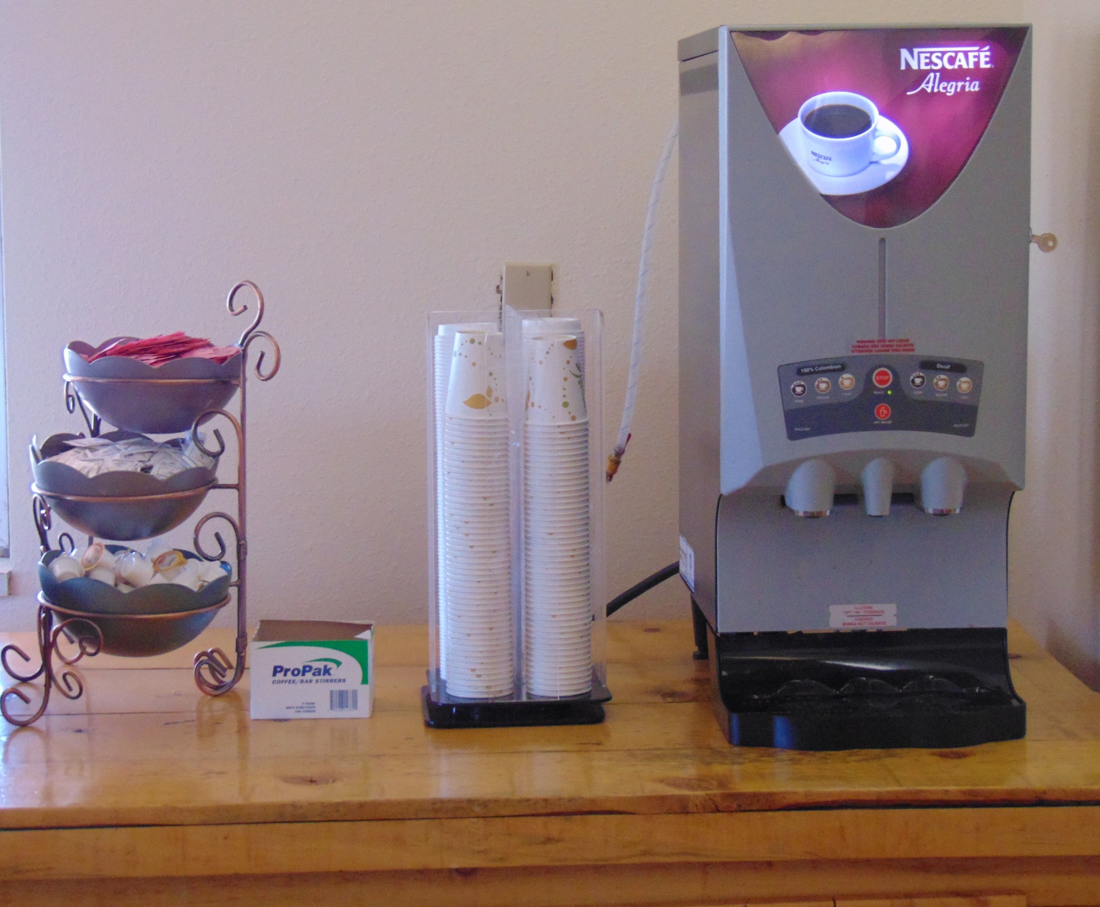 Eine Kaffeemaschine mit Nescafé-Logo, einem Metall-Kaffeedosierer und einer ProPak-Kaffeeumrührstab-Box.