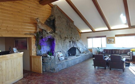 A stone fireplace with a lion statue, a wooden ceiling, a stone wall, a wooden counter, and a seating area with leather chairs.