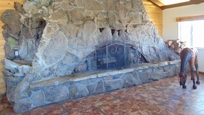 Una chimenea de piedra con rejilla metálica, ubicada en una habitación con paredes de madera y suelo de baldosas.