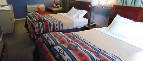 A hotel room with two beds, a desk, a chair, and a nightstand with a lamp.