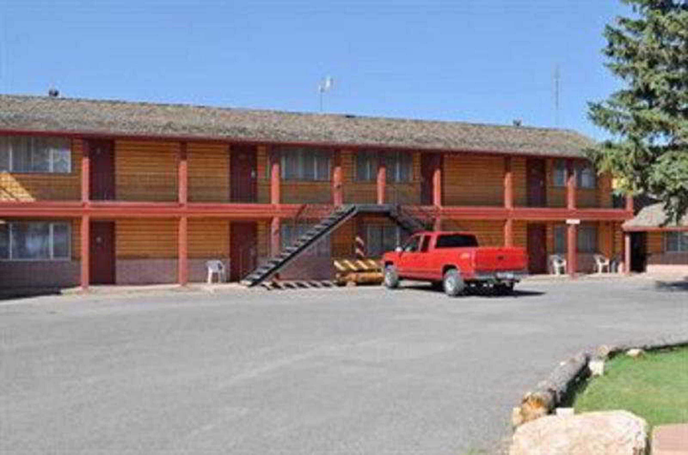 A motel with a red pickup truck parked in front. It has a flat roof and a simple, two-story structure with a covered front porch.