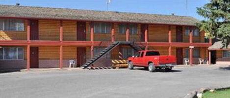 A motel with a red pickup truck parked in front. It has a flat roof and a simple, two-story structure with a covered front porch.