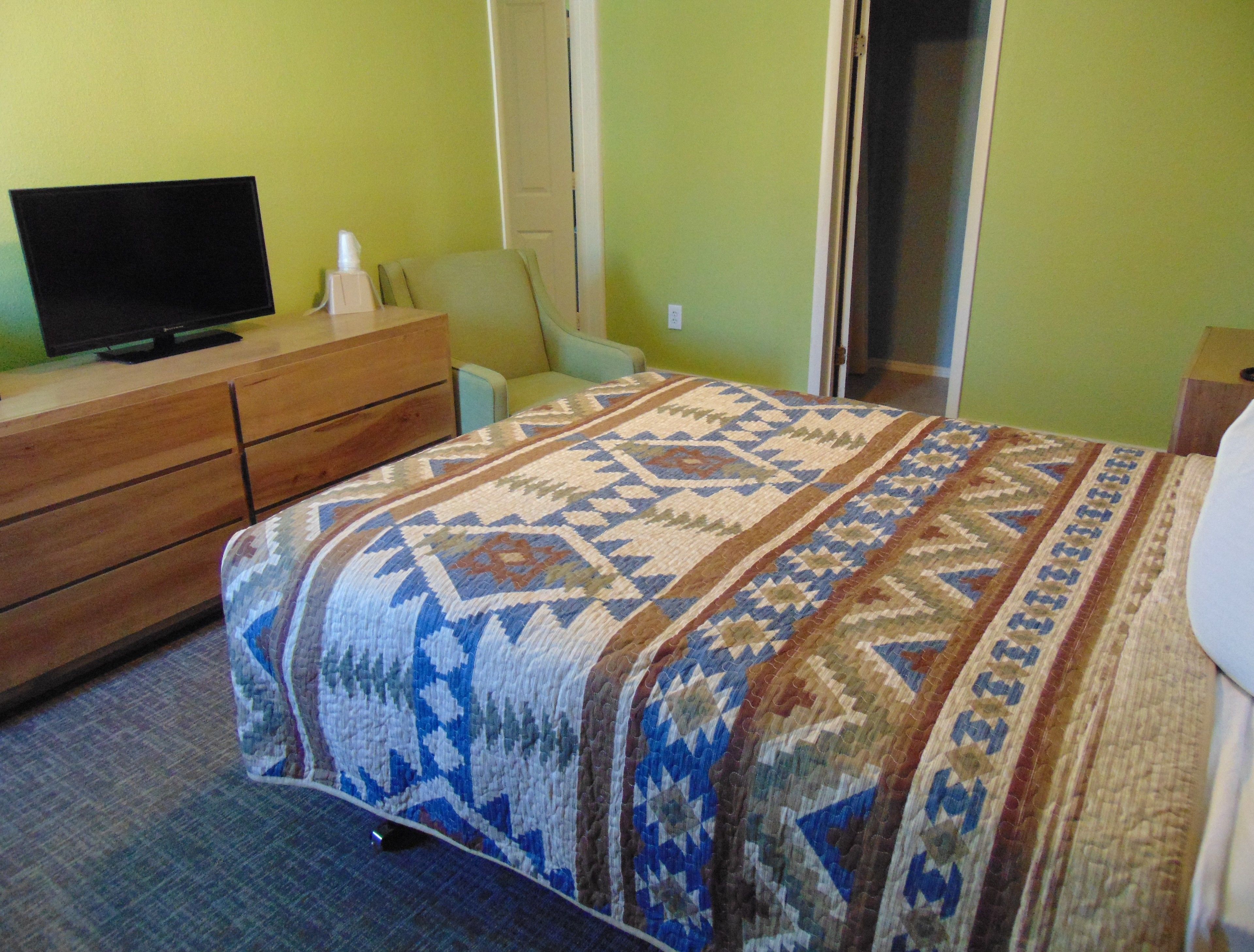 Une chambre d’hôtel avec un lit, une commode en bois, un téléviseur et une porte.