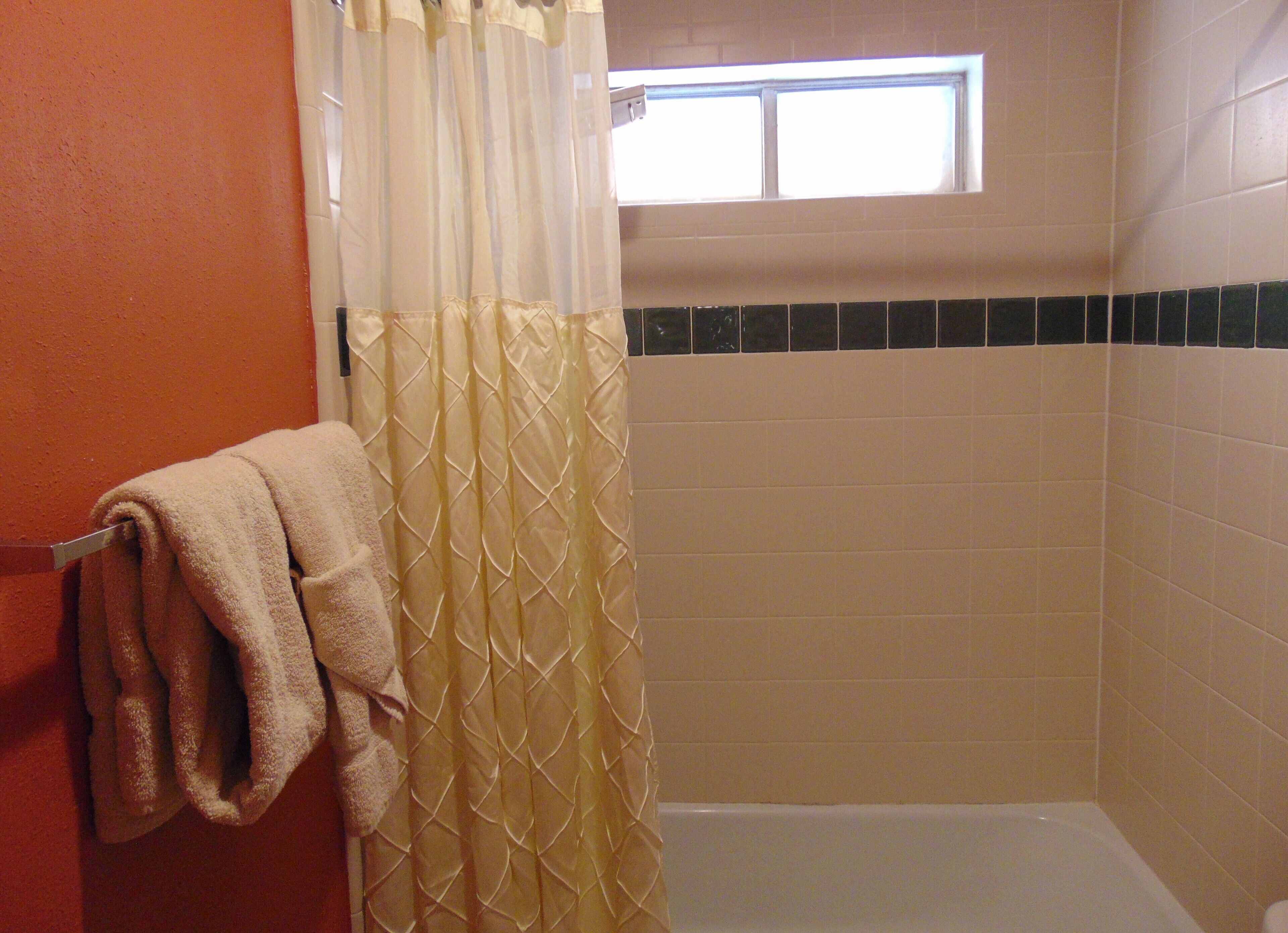 Een badkamer met douchegordijn, een handdoekhouder met handdoek, en een raam boven de douche.