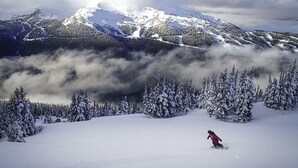 Un paisaje montañoso nevado con una persona practicando snowboard.