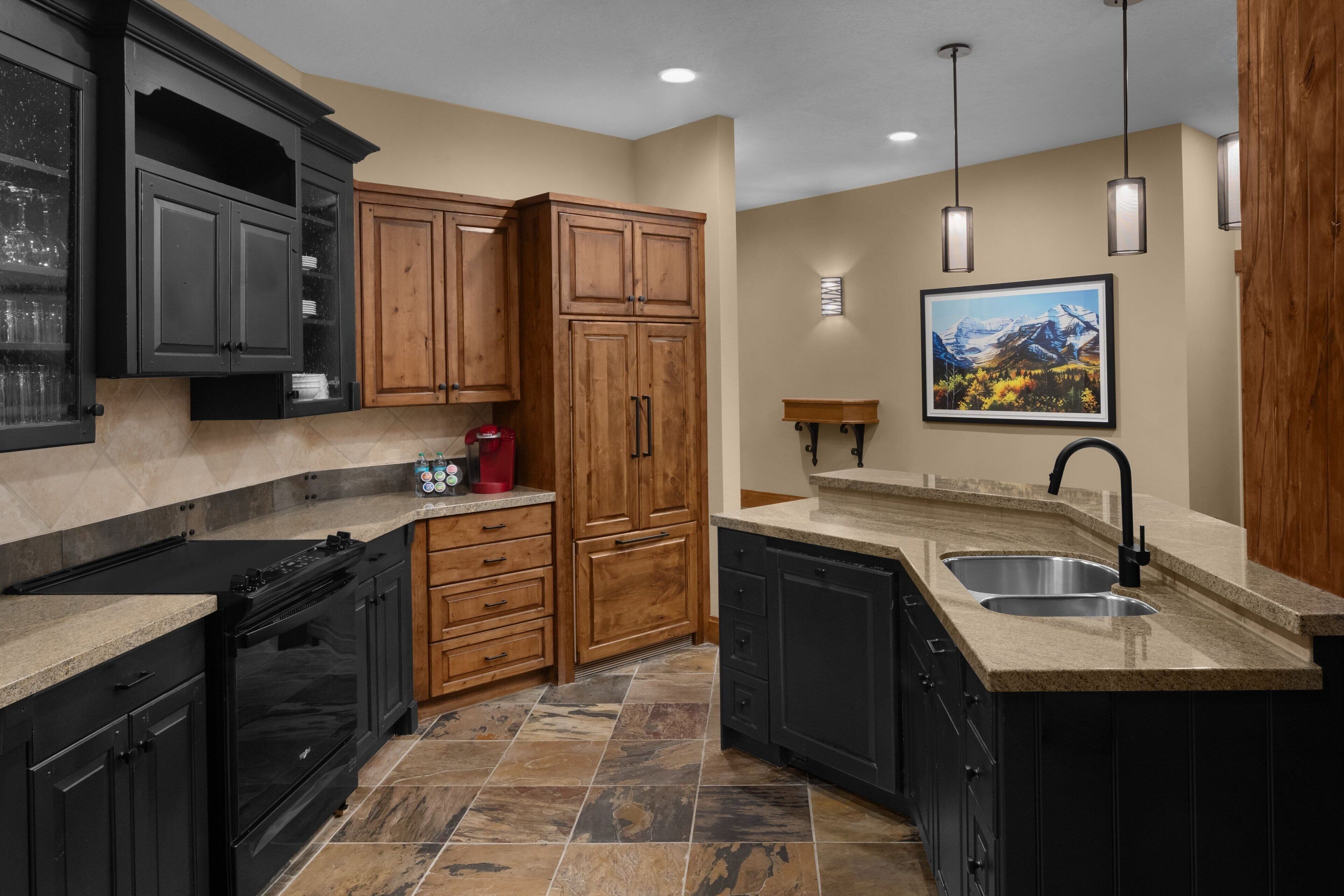 A kitchen with dark cabinets, a granite countertop, a double sink, and a stove.