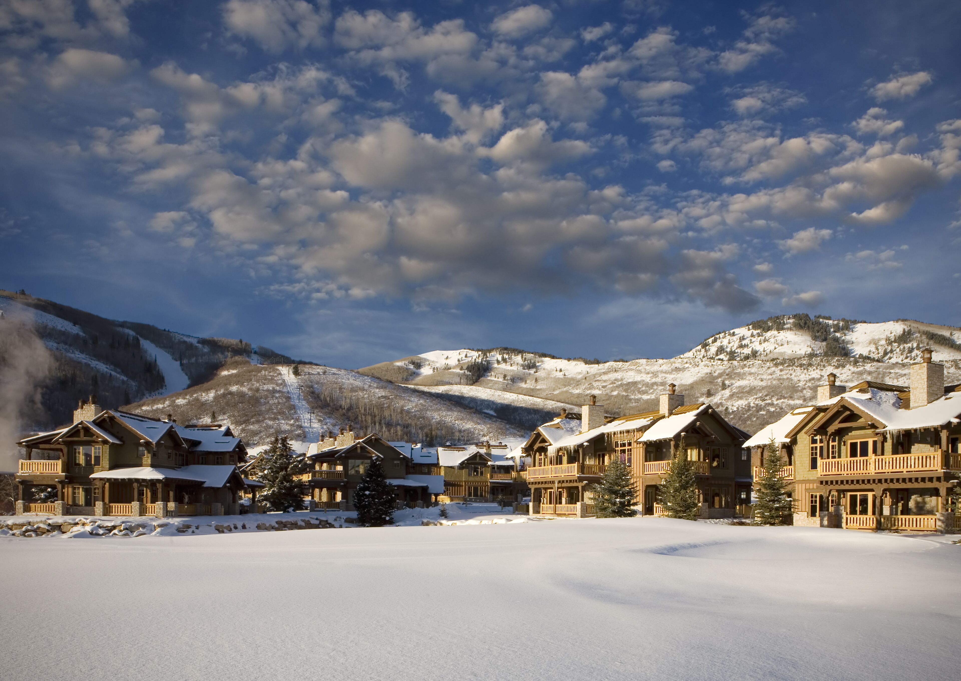 A snow-covered lodge with multiple buildings, a ski slope in the background, and a clear sky.