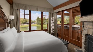 A hotel room with a large bed, a fireplace, a view of a golf course, and a sliding door to an outdoor area.