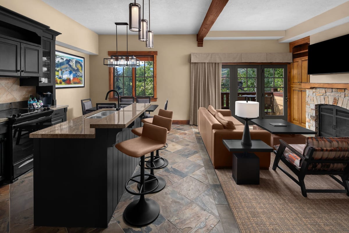 A modern kitchen with a central island, bar stools, and a dining area with a sofa and table.