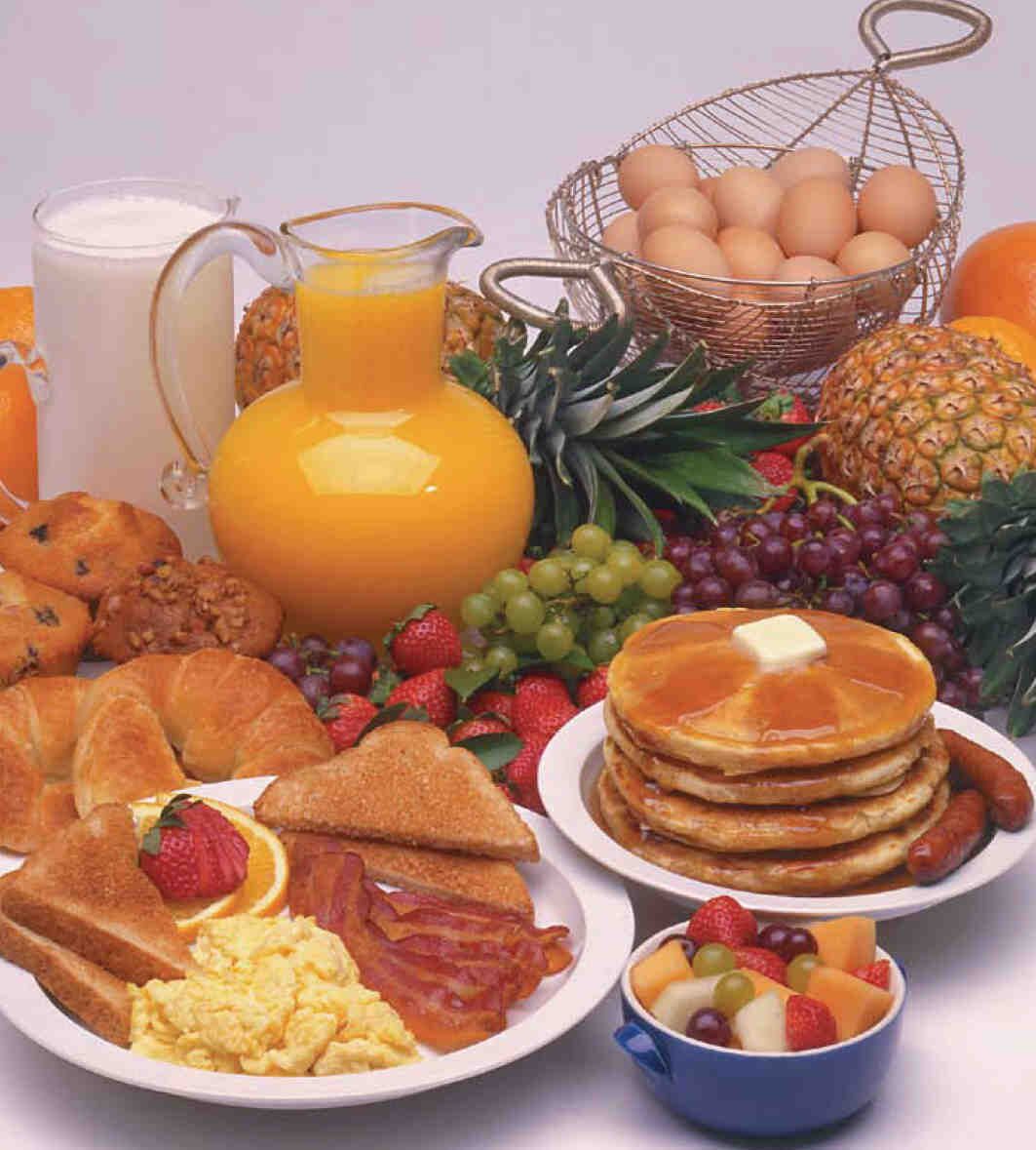 Una mesa con un desayuno abundante de panqueques, huevos, tostadas y fruta.