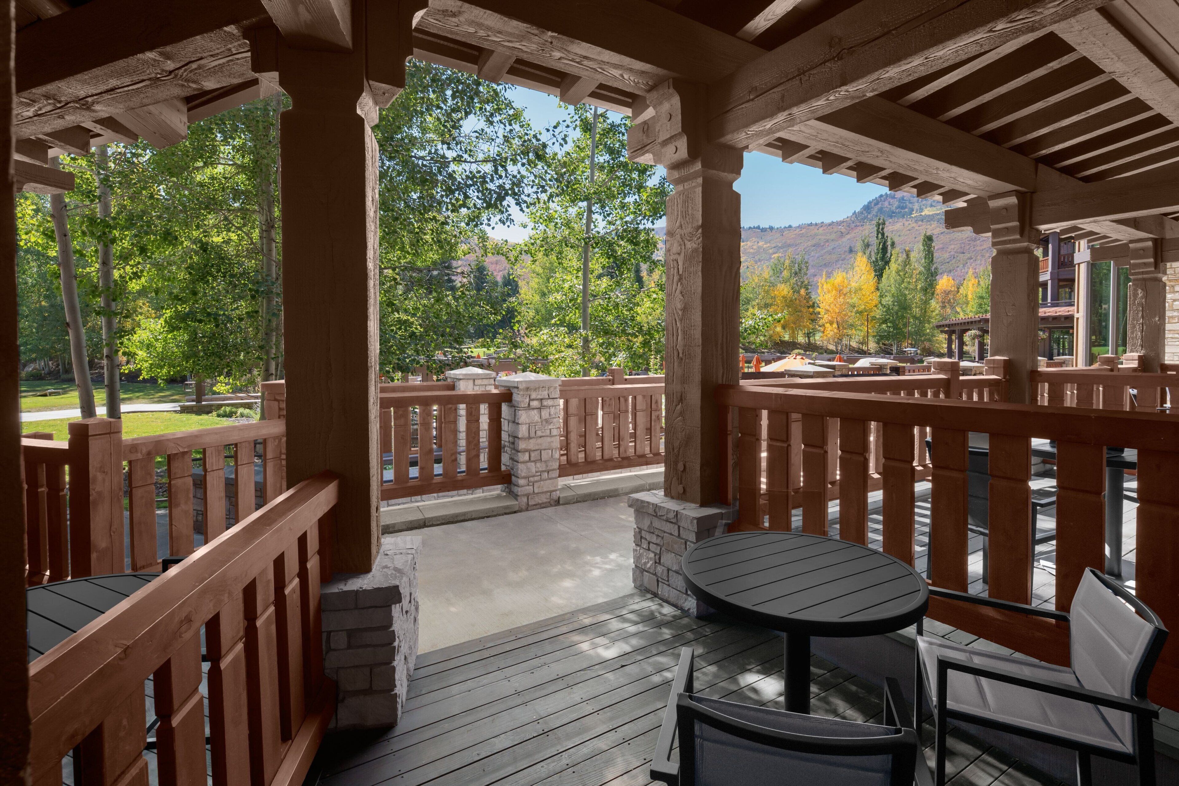 A covered outdoor patio with wooden railings, stone pillars, and a round table with chairs.