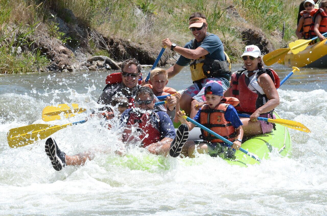 A group of people in a green raft navigating a river.