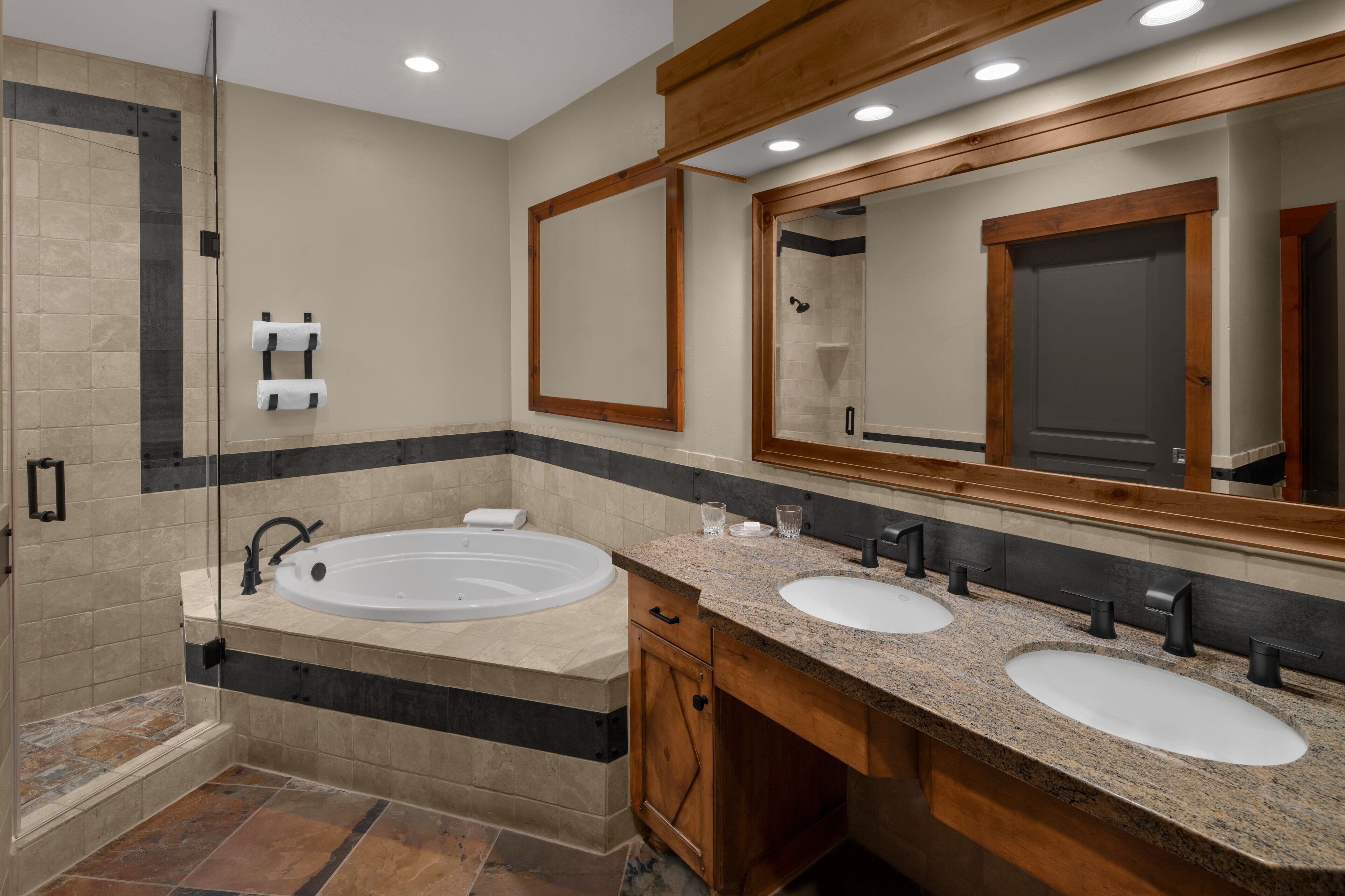 A modern bathroom with a large bathtub, two sinks, and a walk-in shower.