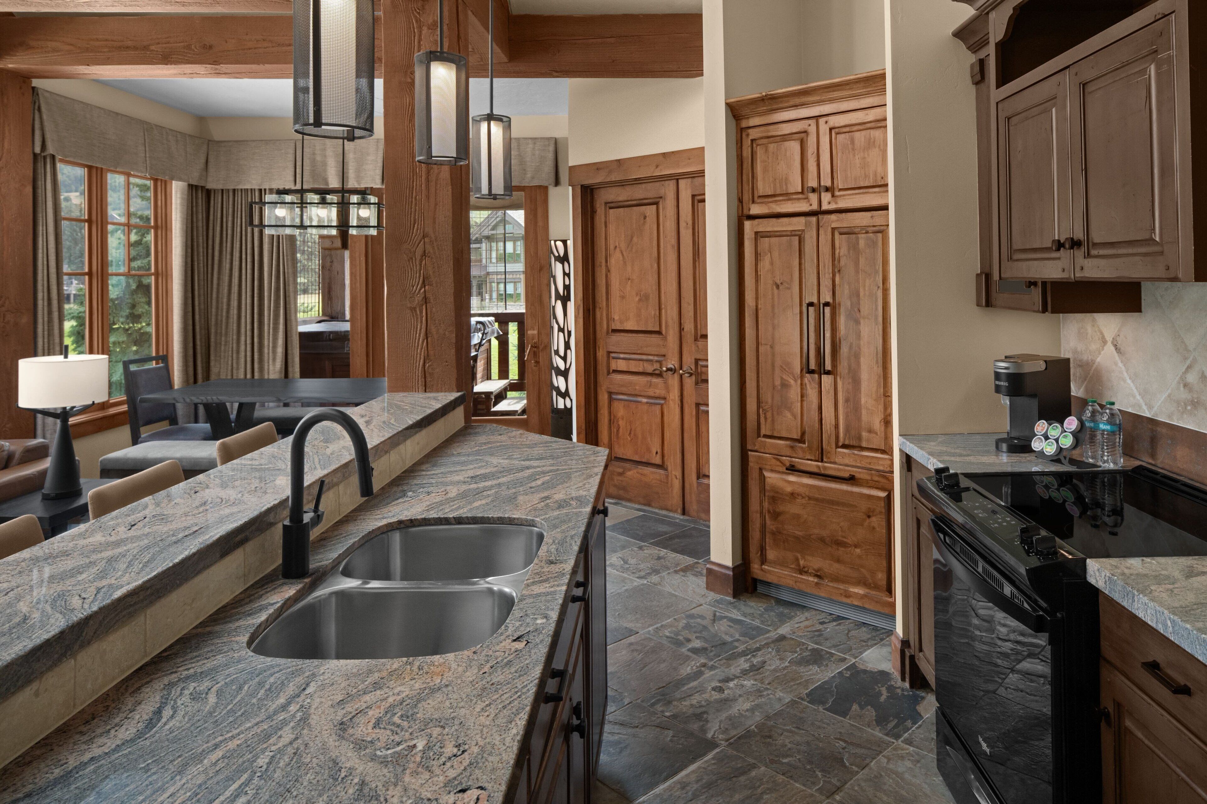 A kitchen with granite countertops, double sinks, wooden cabinets, and a built-in oven.