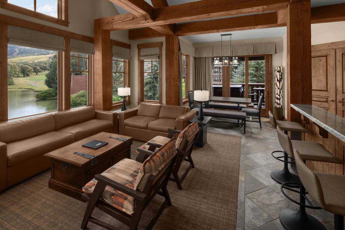 A spacious living room with a large window overlooking a lake, a cozy seating area with a sofa and chairs, and a dining area with a table and chairs.
