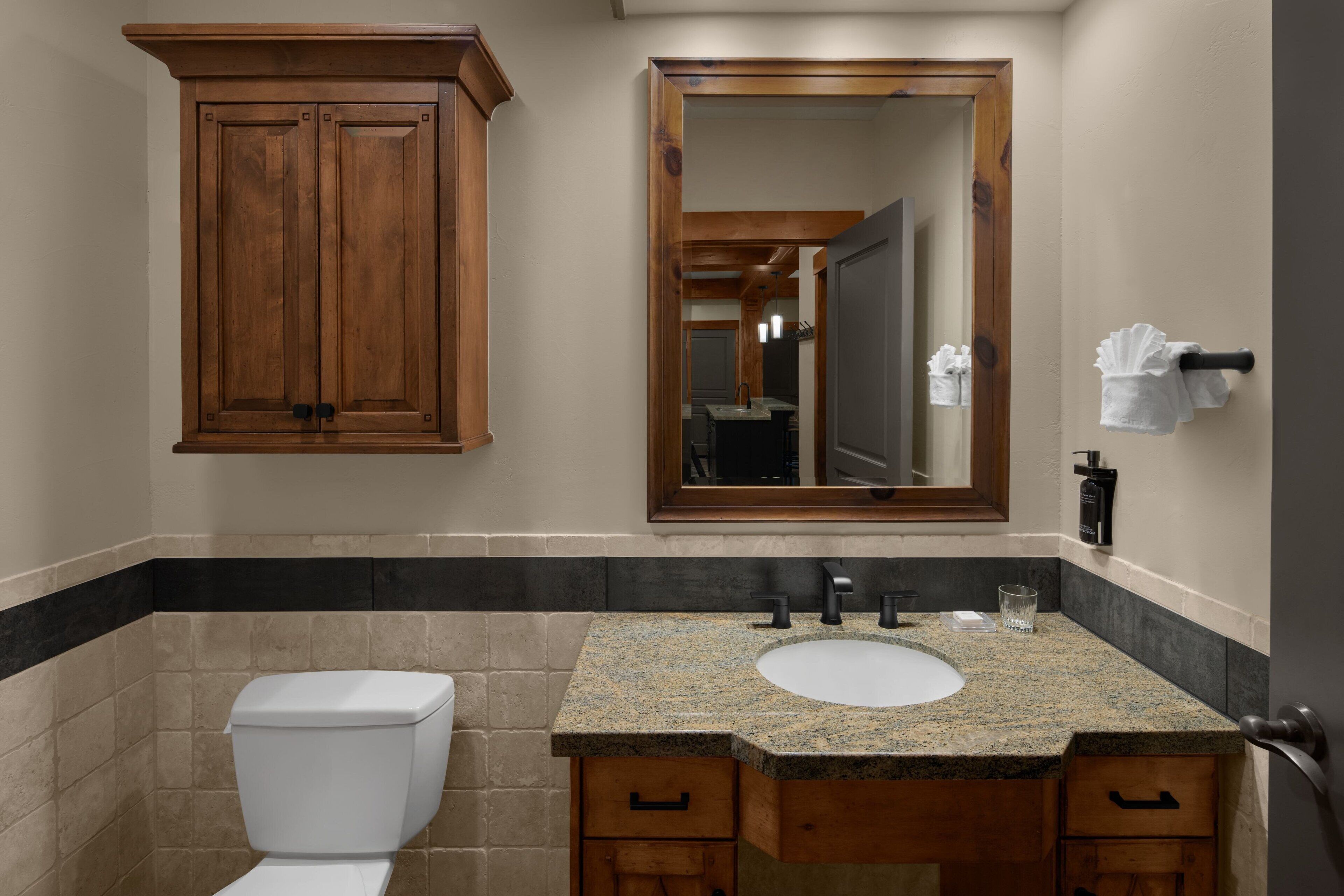 Une salle de bain avec des toilettes blanches, un lavabo sur un plan de travail en granit, des meubles en bois et un grand miroir.