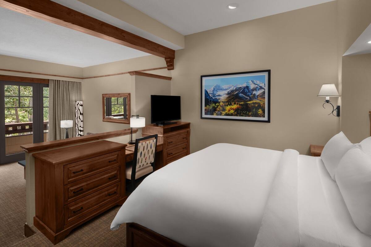 A hotel room with a large bed, wooden dresser, desk, and a television.