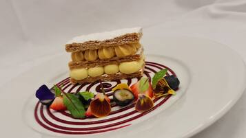 A dessert with multiple layers of cake and cream, garnished with various fruits and leaves on a white plate.