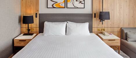 A hotel room with a large bed, two bedside tables, a nightstand, a lamp, a sofa, and two abstract paintings on the wall.