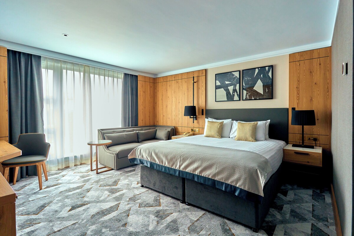 A hotel room with a bed, a sofa, a desk, and a chair.