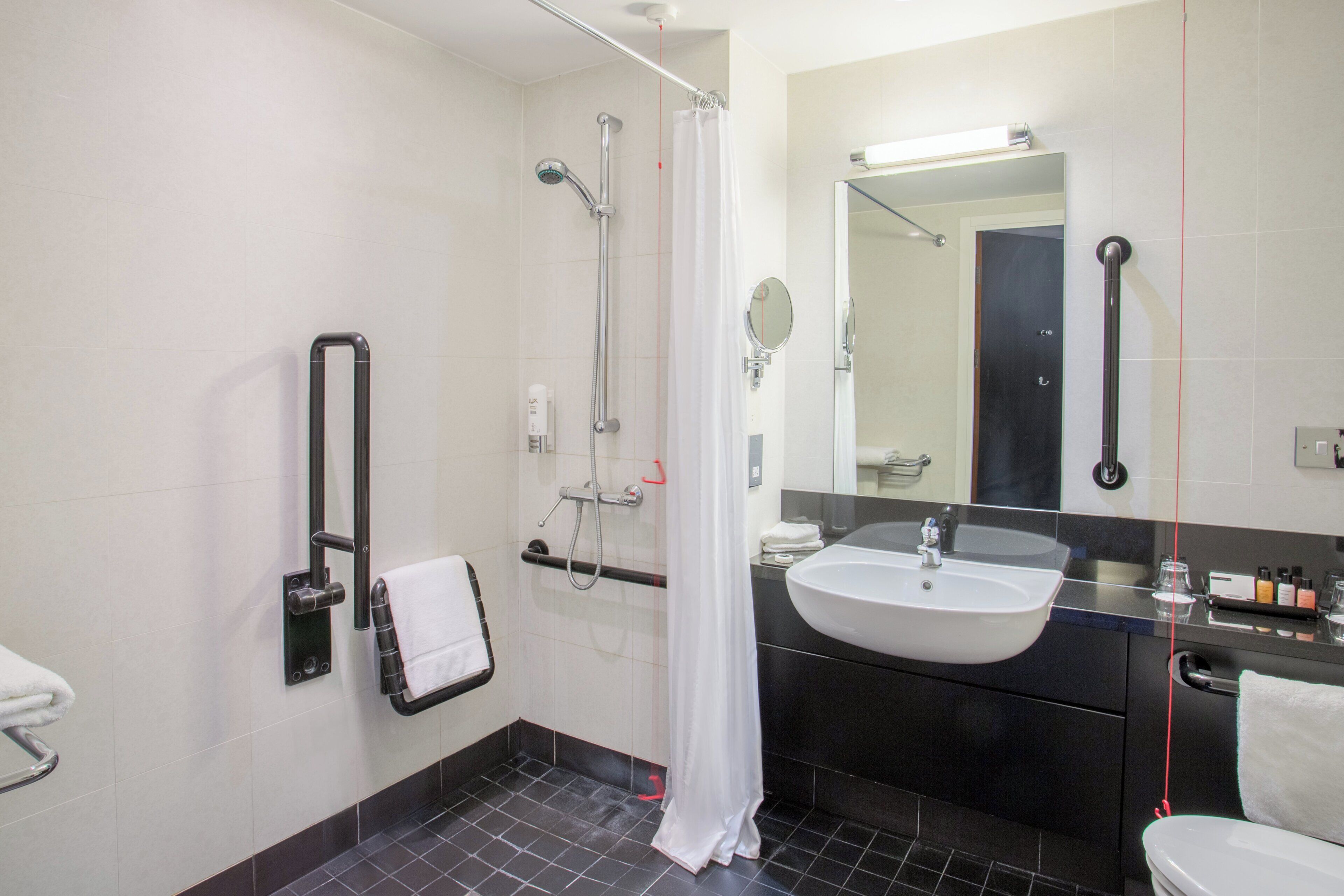 Un baño con ducha, lavabo, espejo y un perchero para toallas.