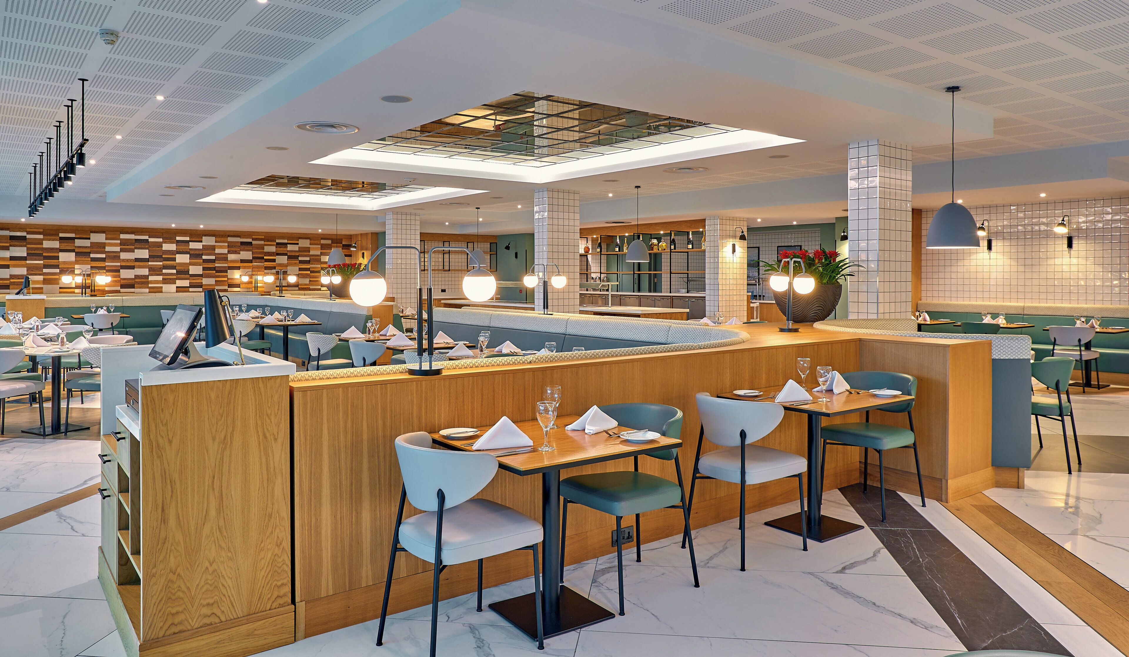 Un restaurante moderno con una barra central, zonas de estar y una cocina al fondo.